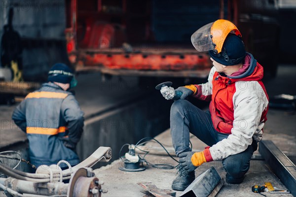 Man worker in a uniform and a mask works with a grinder