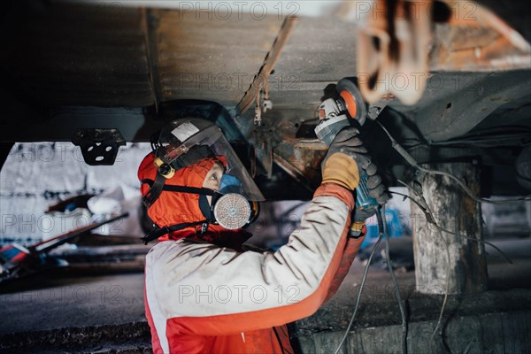 Male car service worker cleans the bottom of the car body with a grinder. Waterproofing metal of a car body