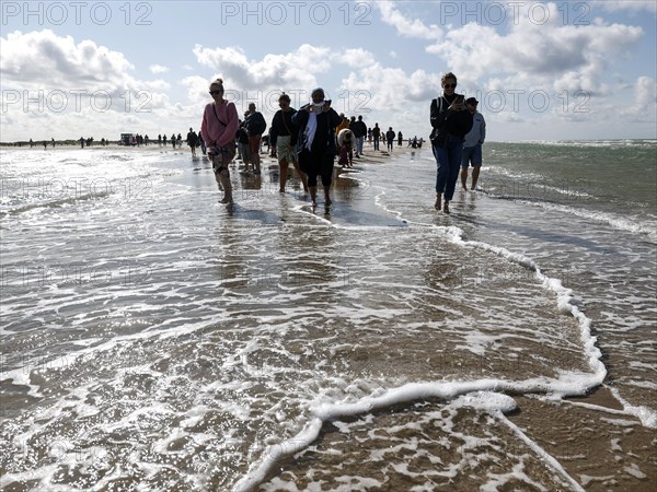 Tourists stand with one foot in the North Sea and one in the Baltic Sea in Grenen or Skagens Gren