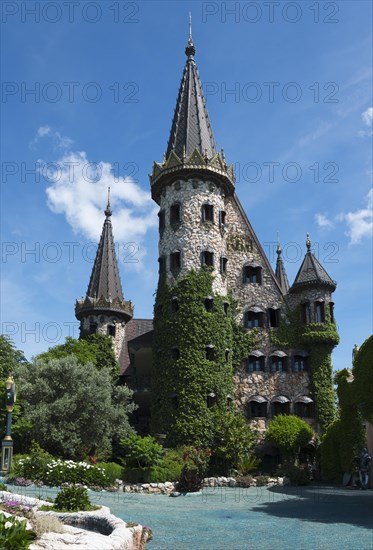 Picturesque castle entwined with ivy under a blue sky with sparse clouds over a small pond