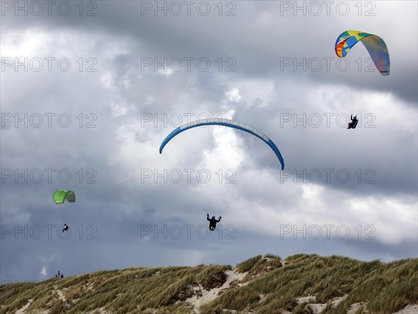 Paragliders flying over a dune landscape on a beach