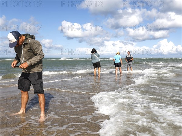 Tourists stand with one foot in the North Sea and one in the Baltic Sea in Grenen or Skagens Gren