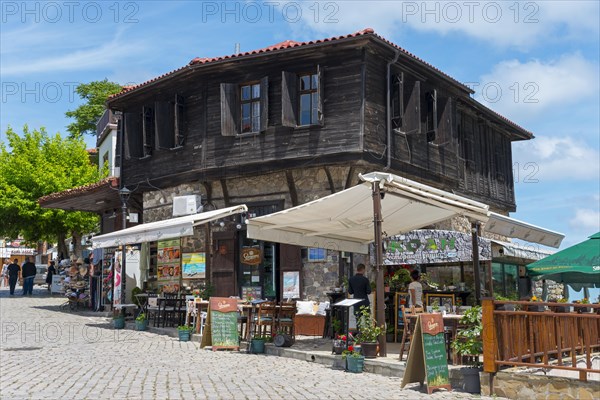 Old wooden house with a street cafe in the foreground under a sunny