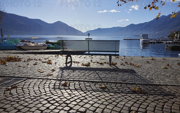 Backlit photograph of a public bench with shade and lake view on the Lungolago