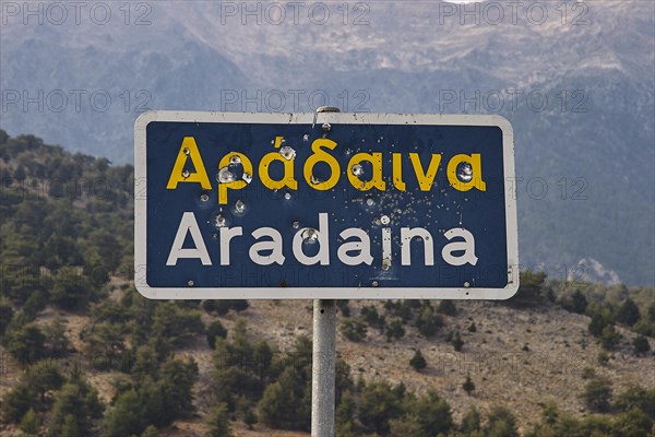 Damaged road sign with Greek and Latin lettering in front of a mountain landscape, Aradena Gorge, Aradena, Sfakia, Crete, Greece, Europe