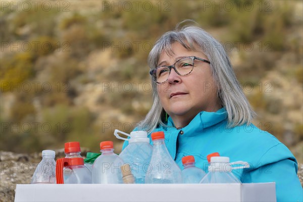 Older white-haired woman holding a cardboard box full of empty plastic bottles collected in the field for recycling, concept of ecology and respect for the environment