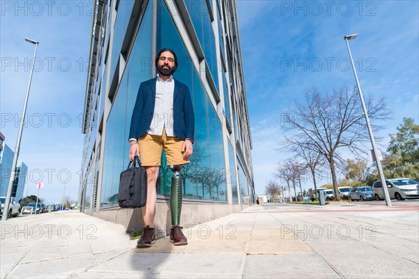 Businessman with prosthetic leg holding a laptop bag outside a financial building in the city