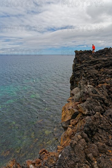 A brave person stands on the edge of a high volcanic cliff above the sea, lava rocks coastal hiking trail Ponta da Iiha, Calhau, west coast, Pico, Azores