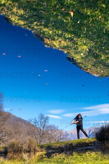 Male Golfer Reflected in a Water Pond and Hitting the Golf Ball on Fairway on Golf Course with Mountain in a Sunny Day in Switzerland