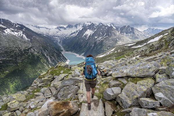 Mountaineer on hiking trail, view of Schlegeisspeicher, glaciated rocky mountain peaks Hoher Weisszint and Hochfeiler with glacier Schlegeiskees, Berliner Hoehenweg, Zillertal Alps, Tyrol, Austria, Europe