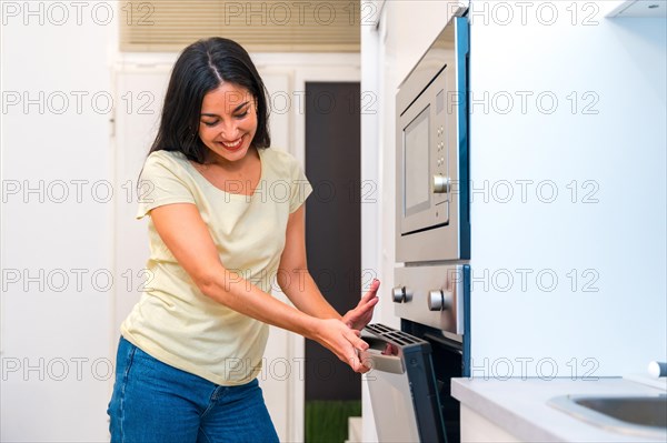 Casual smiling hispanic woman cooking pizza at home in the oven