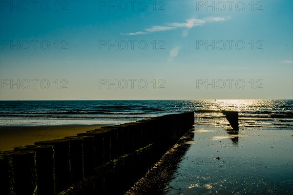 Sun glimmering on ocean water at end of log dividing wall under beautiful blue sky