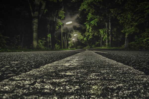 An empty street at night, focussed on the central reservation and surrounded by dark trees, Haan, North Rhine-Westphalia, Germany, Europe