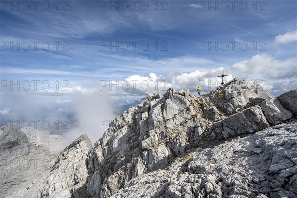 Mountaineer on the rocky summit of the Watzmann Mittelspitze with summit cross, Watzmann crossing, Berchtesgaden National Park, Berchtesgaden Alps, Bavaria, Germany, Europe