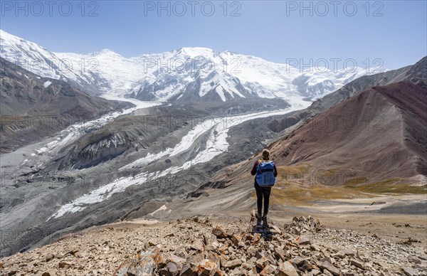 Mountaineer at Traveller's Pass with view of impressive mountain landscape, high mountain landscape with glacier moraines and glacier tongues, glaciated and snow-covered mountain peaks, Lenin Peak and Peak of the XIX Party Congress of the CPSU, Trans Alay Mountains, Pamir Mountains, Osh Province, Kyrgyzstan, Asia