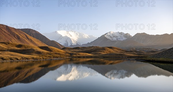 White glaciated and snowy mountain peak Pik Lenin at sunset, mountains reflected in a lake between golden hills, Trans Alay Mountains, Pamir Mountains, Osh Province, Kyrgyzstan, Asia