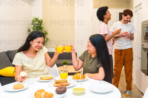 Two women toasting with juice while having breakfast with friends at home