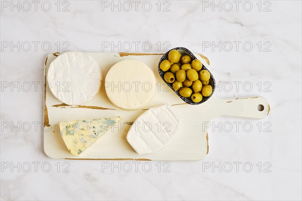 Top view of brie, camembert, goat cheese and cheese with blue mold on white serving board