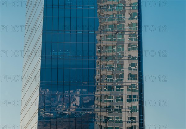 Low angle view of glass office building with reflection of brick building in side windows on sunny day