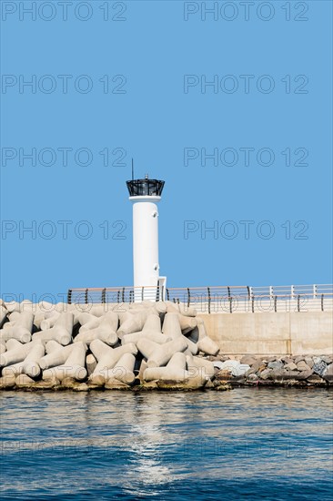 White lighthouse on concrete pier against clear blue sky