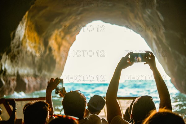 Tourist sightseeing and taking photos with smartphones inside the cave in the Algarve coast, Albufeira, Portugal, Europe