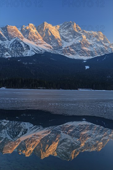 Steep mountains reflected in mountain lake in winter, icy, evening light, Eibsee lake, Zugspitze, Bavaria, Germany, Europe