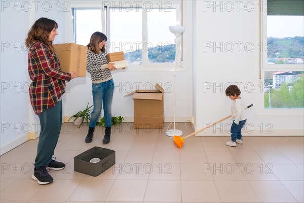 Playful girl distracted while her lesbian mothers move holding and carrying boxes