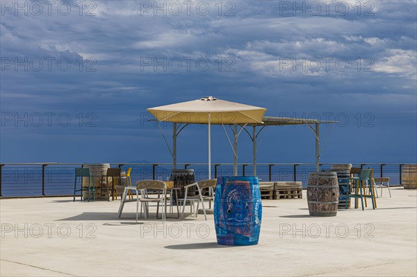 Wine barrels and parasol in front of dark clouds on the terrace of the Tenuta delle Ripalte winery, Elba, Tuscan Archipelago, Tuscany, Italy, Europe