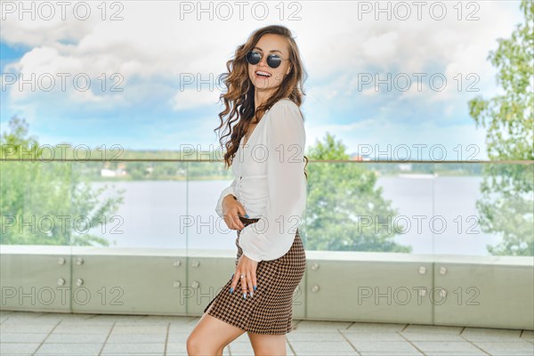 Outdoor portrait of happy young woman in blouse and mini skirt with crow's foot pattern