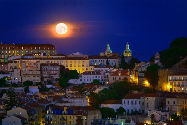 Beautiful view of big full moon over Lisbon areas of Sao Vincente de Fora church, Sao Jorge castle and houses downhill, Portugal. Supermoon, close up, Europe, night, landscape, cityscape, clear sky. Romantic evening, fairy tales, stories