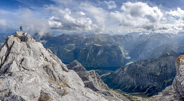 Mountaineer on the rocky summit of the Watzmann Mittelspitze, Watzmann crossing, view of mountain panorama with Steinernes Meer and Koenigssee, Berchtesgaden National Park, Berchtesgaden Alps, Bavaria, Germany, Europe