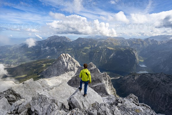 Mountaineer on the rocky summit of the Watzmann Mittelspitze, Watzmann crossing, view of mountain panorama with Steinernes Meer and Koenigssee, Kleiner Watzmann and Watzmann children, Berchtesgaden National Park, Berchtesgaden Alps, Bavaria, Germany, Europe