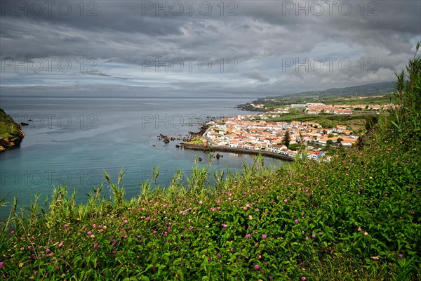 View of the town of Horta surrounded by green hills and cliffs under a cloudy sky, Monte da Guia, Horta, Faial, Azores, Portugal, Europe