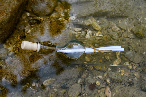 Message in a bottle floating in the water on the rocks at the seashore