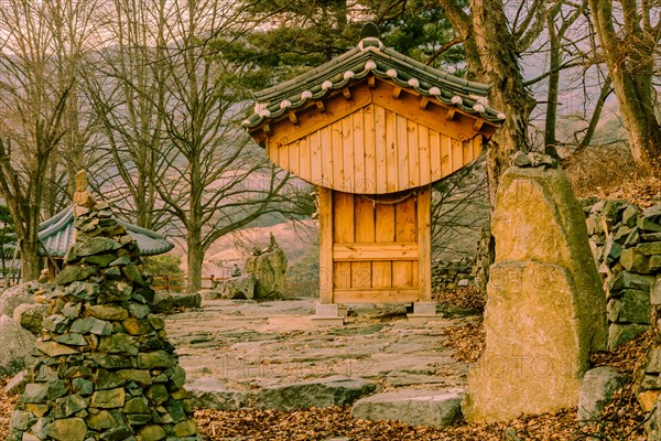 Small wooden oriental building with tiled roof in front of rock wall at countryside roadside park on winter evening