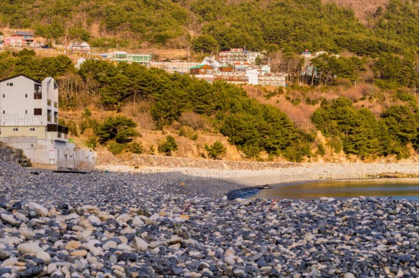 Landscape of Pebble beach in South Korea with buildings on a hill with lush green trees in the background