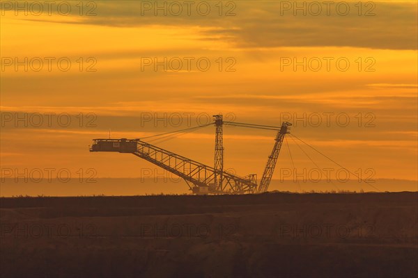 Silhouette of a large conveyor bridge against the orange-coloured evening sky, open-cast lignite mine, North Rhine-Westphalia, Germany, Europe