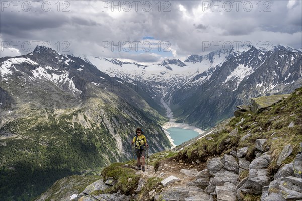 Mountaineer on hiking trail, view of Schlegeisspeicher, glaciated rocky mountain peaks Hoher Weisszint and Hochfeiler with glacier Schlegeiskees, Berliner Hoehenweg, Zillertal Alps, Tyrol, Austria, Europe