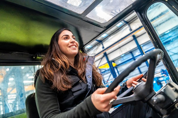 Low angle view close-up of a happy woman driving a forklift in a factory