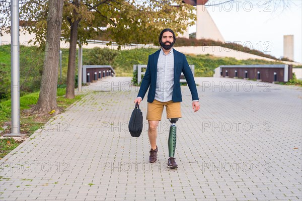 Frontal view of a businessman with prosthetic leg carrying laptop bag along an urban park