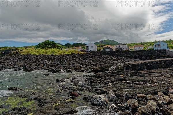 Landscape with volcanic rock formations and scattered houses under a cloudy sky, lava rocks Coastal hiking trail Ponta da Iiha, Calhau, west coast, Pico, Azores