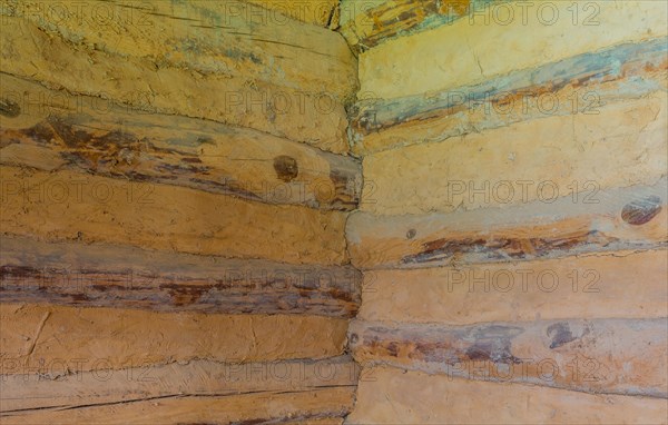 Interior corner of two walls of log cabin made of logs and held together with dried mud