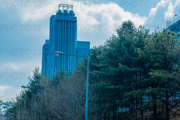 Low angle view of tall industrial building on tree lined street near Daejeon, South Korea under cloudy sky. Building is part of local brewery