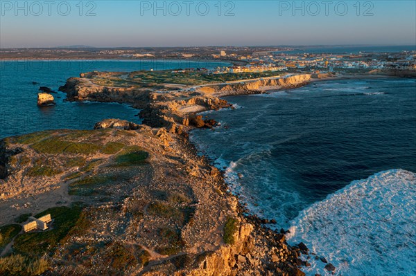 Sunset landscape of peninsula, bay and town of Peniche, Portugal. Summer sunset haze, little foliage and rocky cliffs, peninsula and rocks, fishing town, horizon, aerial shot, drone point of view