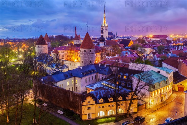 Aerial view of Tallinn Medieval Old Town with St. Olaf's Church and Tallinn City Wall illuminated in evening with dramatic cloudscape, Estonia, Europe