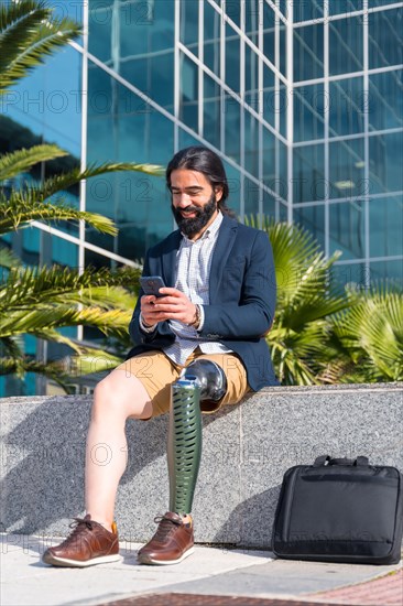 Vertical portrait of a businessman with prosthetic leg using mobile sitting outside a financial building