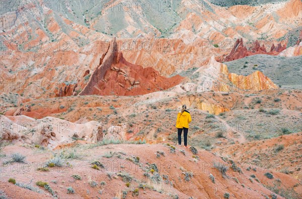 Hiker in front of eroded mountain landscape, sandstone cliffs, canyon with red and orange rock formations, Konorchek Canyon, Chuy, Kyrgyzstan, Asia