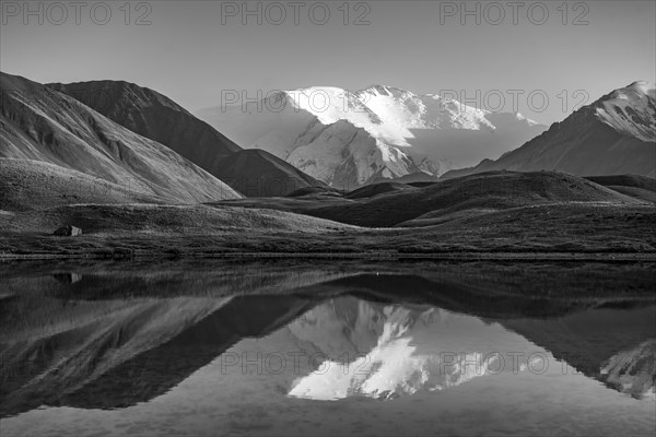 White glaciated and snowy mountain peak Lenin Peak at sunset, mountains reflected in a lake between golden hills, black and white photograph, Trans Alay Mountains, Pamir Mountains, Osh Province, Kyrgyzstan, Asia