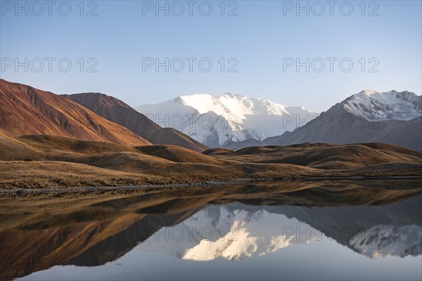 White glaciated and snowy mountain peak Pik Lenin at sunset, mountains reflected in a lake between golden hills, Trans Alay Mountains, Pamir Mountains, Osh Province, Kyrgyzstan, Asia