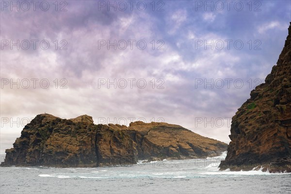 Rocky island 'Iieu Deitado' under a dramatic cloudy sky with gentle waves at the base, Iieu Deitado, Iieu em Pe, Horta, Faial, Azores, Portugal, Europe